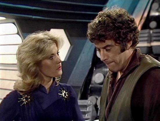 Claude 3.7 describes the image as: "This image shows a scene set in what appears to be a spacecraft interior with distinctive futuristic design elements typical of classic science fiction television from the late 1970s/early 1980s. 

The scene features two individuals in conversation - a person with blonde feathered hair wearing a navy blue outfit with decorative gold accents on the shoulders, and another person with curly dark hair wearing a brown jacket over darker clothing.

The spacecraft s…