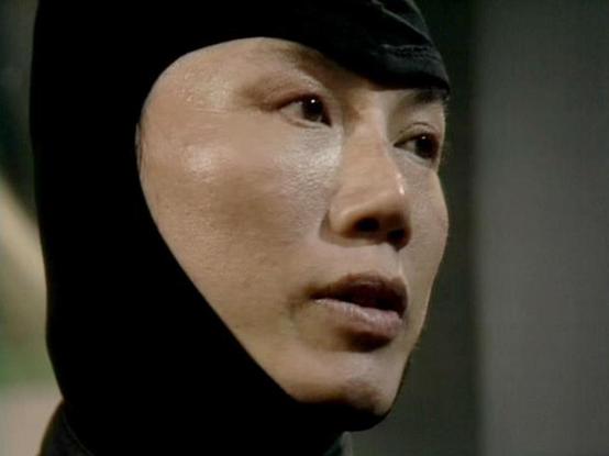 Claude 3.7 describes the image as: "The image appears to be from a television production showing a person wearing what looks like a black head covering or hood. The lighting creates a dramatic effect, highlighting the contours of their face against the darker background. The person has an intense, focused expression and appears to be in a serious scene. The costume suggests this might be from a science fiction or action production, possibly depicting a character in some type of tactical or spec…