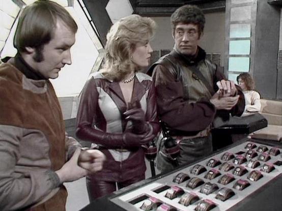 Claude Sonnet 4.0 describes the image as: "This appears to be a scene set aboard a spacecraft, likely the Liberator, showing crew members gathered around what looks like a control console or computer interface. The setting has the characteristic futuristic interior design of the series, with metallic surfaces and technological equipment visible in the background. The characters appear to be examining or discussing something displayed on a screen or panel, which shows a grid of what might be dat…