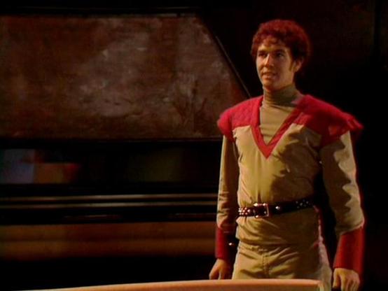 Claude Sonnet 4.0 describes the image as: "I can see a figure in what appears to be a futuristic or science fiction setting, wearing distinctive costume elements including red and tan/brown colored clothing with a cape-like garment. The character appears to be on what looks like a spaceship or futuristic interior set, with curved walls and technological elements visible in the background. The lighting creates a dramatic atmosphere typical of science fiction television productions from this era.…