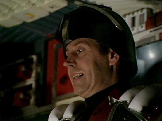 Claude 3.7 describes the image as: "This image appears to be from a science fiction television production, showing a person in what looks like a military or security uniform with a distinctive black helmet. They appear to be inside what could be a spacecraft or command center, with technical equipment and panels visible in the background. The scene has a somewhat dark, industrial aesthetic with red and metallic elements visible in the background, which was characteristic of many sci-fi producti…