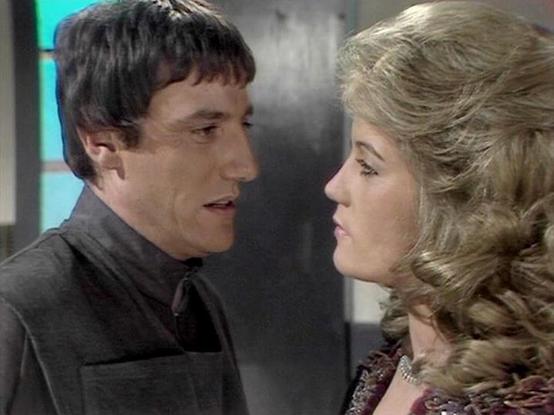 Claude Sonnet 4.0 describes the image as: "I can see this appears to be from a science fiction television production, likely from the late 1970s or early 1980s based on the styling and production values. The scene shows two characters in what appears to be an intimate or tense moment - a dark-haired man in black clothing facing a blonde woman with an elaborate curled hairstyle typical of that era. The setting appears to be some kind of futuristic interior space, possibly a spacecraft or station…