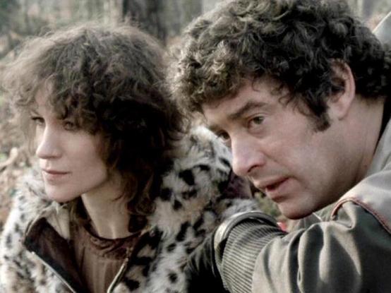 Claude 3.7 describes the image as: "The image shows two individuals with curly dark hair in what appears to be a rustic or wilderness setting. They are wearing what looks like period or specialized costume clothing, with one wearing what appears to be a spotted fur or animal print garment. The scene has a muted, somewhat desaturated color palette typical of television productions from the late 1970s or early 1980s.

The individuals seem to be in a tense or watchful moment, with one looking off …