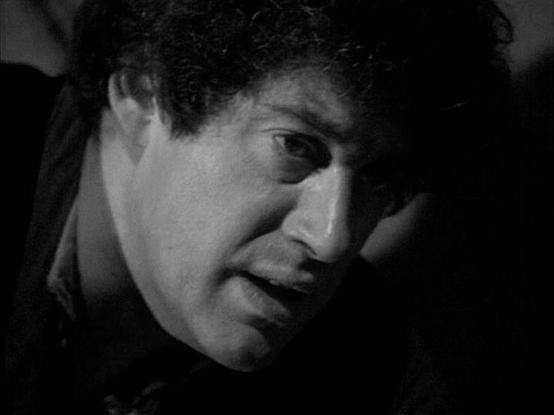 Claude Sonnet 4.0 describes the image as: "I can see this is a black and white dramatic close-up shot that appears to be from a television production, likely from the late 1970s or early 1980s based on the visual style and production quality. The lighting creates strong shadows and contrast, giving the scene a moody, intense atmosphere typical of dramatic moments in science fiction television of that era. The composition focuses tightly on the subject, suggesting this may be capturing an import…
