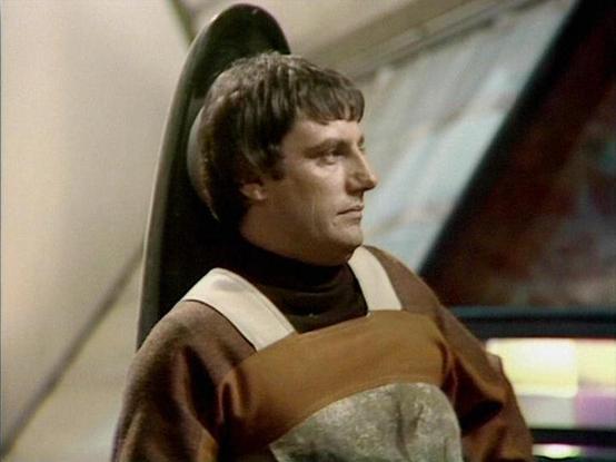 Claude Sonnet 4.0 describes the image as: "This image shows a scene from inside a spacecraft, with futuristic interior design elements visible in the background. The character appears to be in a contemplative or brooding pose, wearing what looks like a distinctive costume with earth-toned colors and geometric patterns typical of science fiction television from this era. The setting suggests this is taking place aboard one of the main vessels featured in the series, with the sleek, angular archi…