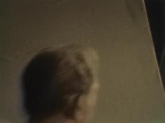 Claude 3.7 describes the image as: "This image appears to be quite blurry and low quality, making it difficult to clearly identify details. It shows what seems to be a person in dim lighting against a plain wall background. The image has a grainy, possibly vintage quality that could be consistent with footage from an older television series. Due to the poor resolution and lighting conditions, specific details about the setting or context are not easily discernible. The color palette appears to …