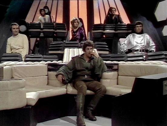 Claude Sonnet 4.0 describes the image as: "This appears to be a scene set in the crew quarters or common area of a spacecraft, featuring several characters in a tiered, futuristic interior with white seating and metallic surfaces. The setting has a sterile, high-tech aesthetic typical of science fiction productions from this era. The characters are positioned at different levels - some seated on elevated platforms in the background, while one figure sits prominently on the white curved seating …