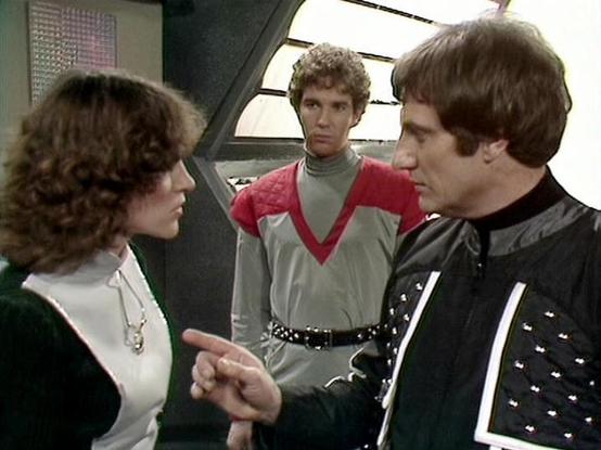 Claude Sonnet 4.0 describes the image as: "This appears to be a scene set aboard the Liberator spacecraft, showing three crew members in what looks like a tense discussion or confrontation. The setting is the ship's flight deck or control room, characterized by its distinctive futuristic interior design with curved walls and control panels visible in the background.

The woman on the left has curly dark hair and is wearing a white top with a dark outer garment. She appears to be gesturing as sh…