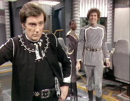 Claude Sonnet 4.0 describes the image as: "This appears to be a scene set aboard a spacecraft, likely the Liberator or Scorpio based on the futuristic interior design with metallic walls and technical equipment visible in the background. The setting has the characteristic sterile, high-tech aesthetic typical of the series' spaceship environments.

In the foreground, a character wearing distinctive black leather clothing with decorative studs and buckles is prominently featured. This appears to …