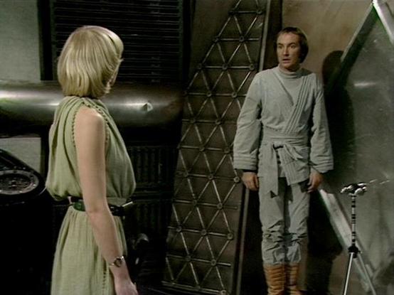 Claude 3.7 describes the image as: "The image shows a scene set in what appears to be a futuristic or sci-fi environment with metallic walls and geometric patterns. Two people are visible in the frame - one wearing a light green sleeveless dress with blonde hair on the left, and another in a light gray wraparound tunic with matching pants and tan boots on the right.

The setting has a distinctive retro sci-fi aesthetic typical of British television productions from the late 1970s/early 1980s. T…