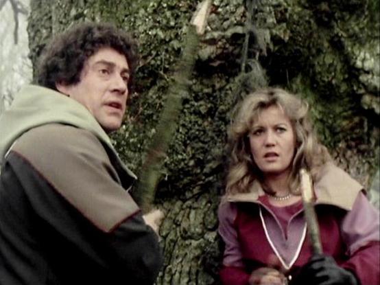 Claude 3.7 describes the image as: "This image appears to be a still from a vintage British science fiction television series from the late 1970s or early 1980s. The scene shows two people in what looks like a forest or wooded area. On the left is a person wearing a dark and olive-colored jacket, with curly dark hair. On the right is a person with blonde wavy hair wearing a pink and burgundy outfit with a light-colored collar. Both appear to have concerned or alarmed expressions on their faces …