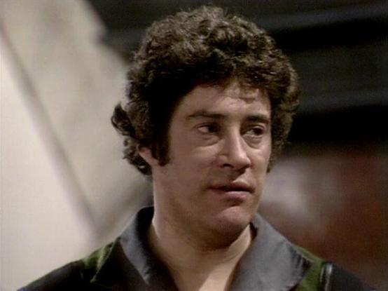 Claude Sonnet 4.0 describes the image as: "I can see this appears to be from a science fiction television production, likely from the late 1970s or early 1980s based on the image quality and styling. The scene shows someone in what appears to be a futuristic or military-style costume with distinctive collar details. The setting looks like it could be aboard a spacecraft or in some kind of technical facility, with blurred background elements suggesting an industrial or high-tech environment. The…