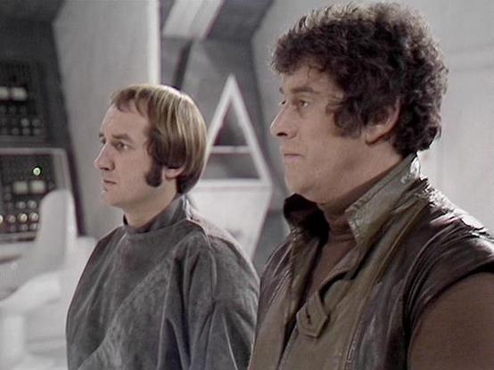 Claude Sonnet 4.0 describes the image as: "I can see this is a scene set in what appears to be a futuristic spacecraft interior, with characteristic white walls and technological equipment visible in the background. The setting has the distinctive sterile, high-tech aesthetic typical of science fiction productions from this era. Two characters are present in the scene - one wearing darker clothing and another in lighter garments. The composition and lighting suggest this is from a dramatic mome…