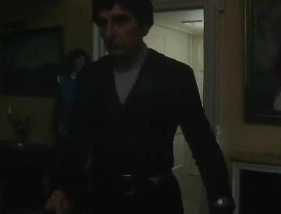 Claude 3.7 describes the image as: "The image shows a person in a dark interior setting, wearing what appears to be a black outfit or uniform with a v-neck. The lighting is very dim, giving the scene a moody, dramatic atmosphere. The background reveals what looks like a corridor or room in what might be a spacecraft or facility, with light-colored walls visible. 

The aesthetic has that distinctive late 1970s/early 1980s British television production quality - somewhat grainy and darkly lit. Th…