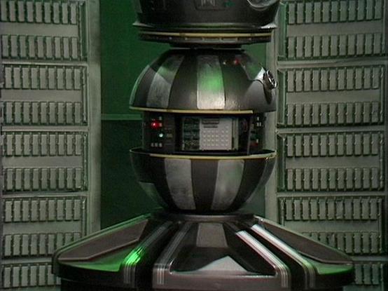 Claude 3.7 describes the image as: "This image shows a droid or robot character from the science fiction television series. The machine has a distinctive spherical, segmented design with metallic sections separated by gold trim bands. It appears to have a control panel with small red lights visible in its midsection. The robot is positioned in what looks like a technical corridor or facility with textured green wall panels visible on either side, creating a classic retro sci-fi aesthetic. The s…