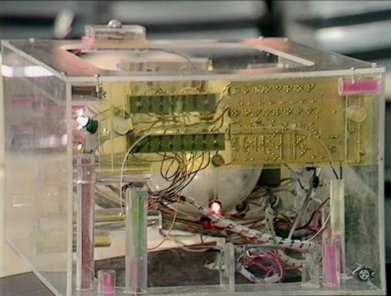 Claude 3.7 describes the image as: "This image shows a clear acrylic or plastic enclosure containing electronic components. Inside the case, there's a visible circuit board (PCB) with a yellowish-green color mounted near the top. The PCB has various electronic components soldered to it and multiple wires connecting different parts of the assembly.

The enclosure appears to be a custom-built prototype or demonstration unit, with pink or reddish structural supports visible at the corners. Various…