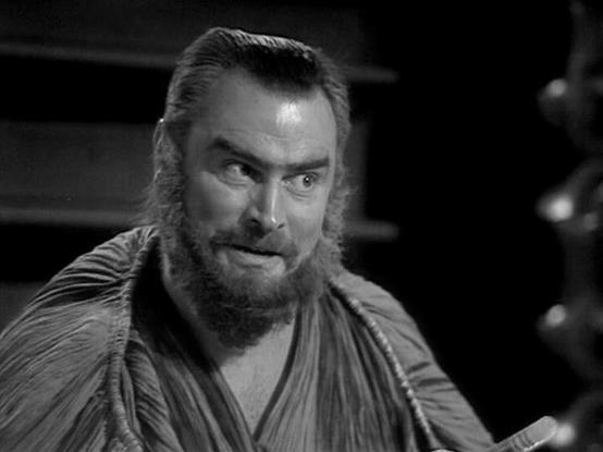 Claude 3.7 describes the image as: "# Image Description

This black and white photograph shows a bearded man with distinctive facial hair in what appears to be a scene from a classic film or television production. The image captures him in a dramatic moment, with an intense expression on his face. He's wearing what looks like period costume - a draped garment with vertical pleating or ridged fabric typical of classical or historical drama productions.

The lighting and cinematography are charac…