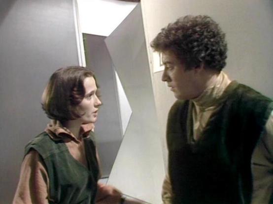 Claude Sonnet 4.0 describes the image as: "I can see this appears to be from a science fiction television production, likely from the late 1970s or early 1980s based on the aesthetic and production values. The scene takes place in what looks like a futuristic, sterile interior setting with white/gray geometric walls and angular architectural elements typical of sci-fi set design from that era.

Two actors are shown in what appears to be an intense dramatic moment. One person on the left has sho…