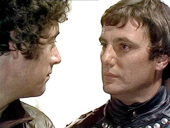 Claude 3.7 describes the image as: "# Scene Description

This image captures an intense face-to-face confrontation between two men against a stark white background. The scene appears to be from a science fiction production, suggested by the distinctive costume elements visible—particularly the studded black leather jacket worn by the man on the right, which has a distinctly futuristic aesthetic.

The man on the left has curly, dark hair and wears what appears to be a brown or tan-colored garmen…