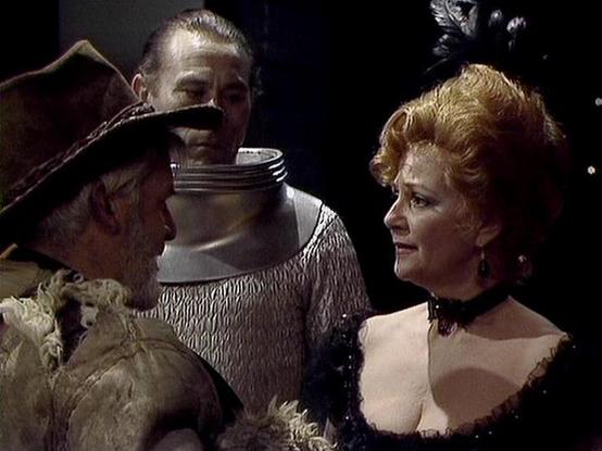 Claude Sonnet 4.0 describes the image as: "I can see this appears to be from a period drama or historical film, showing what looks like a scene with characters in elaborate period costumes. There's someone wearing what appears to be medieval or Renaissance-era armor with a helmet, and a woman in an ornate dress with period styling including an elaborate hairstyle and jewelry. The lighting and cinematography suggest this is from a professional film production, with dramatic lighting against a da…