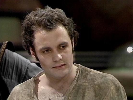 Claude Sonnet 4.0 describes the image as: "I can see this is a still image from what appears to be a film or television production. The image shows a man with curly brown hair wearing what looks like a beige or tan colored sweater or cardigan. The setting appears to be indoors with dim lighting in the background. The image quality and styling suggests this is from an older production, possibly from several decades ago. The person appears to be in character for whatever role they're playing in t…