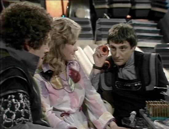 Claude Haiku 4.5 describes the image as: "# Image Description

This scene appears to be from a science fiction television production, likely from the 1970s based on the visual style and set design. The image shows four people in what appears to be a spacecraft interior, characterized by the futuristic but modest production design typical of that era.

The setting features sleek, minimalist backgrounds with geometric patterns and metallic tones. The actors are wearing stylized costumes consisten…