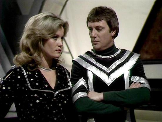 Claude Sonnet 4.5 describes the image as: "This image captures a scene from the classic British science fiction television series "Blake's 7," which aired from 1978 to 1981. The setting appears to be aboard the Liberator spacecraft, characterized by its distinctive angular, modernist interior design with clean lines and geometric shapes visible in the background.

Sally Knyvette portrays Jenna Stannis, a smuggler and pilot who becomes part of the rebel crew. She wears a black outfit adorned wit…