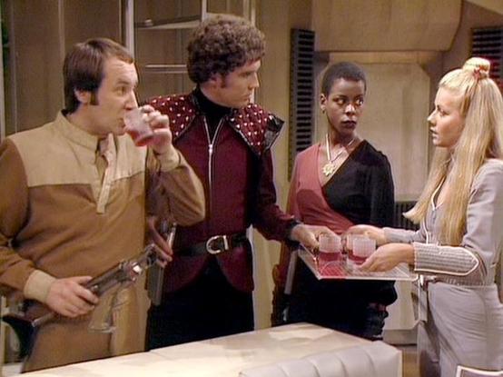 Claude Haiku 4.5 describes the image as: "# Scene Description

This image captures a scene set in what appears to be a futuristic spacecraft interior, characterized by beige and tan walls with metallic fixtures and ventilation panels typical of 1980s science fiction production design. The setting suggests a command or operations area.

Five individuals are present in the scene, engaged in what appears to be an intense conversation or confrontation. The person on the far left wears a tan/beige t…