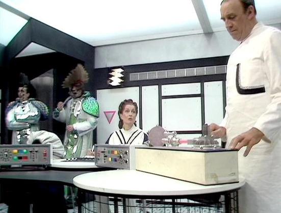 Claude Haiku 4.5 describes the image as: "# Image Description

This appears to be a scene from a science fiction television production, likely from the 1970s or 1980s based on the styling and set design. The setting is a futuristic control room or command center, featuring distinctive retro-futuristic decor with geometric shapes and bold color blocking in black, white, and green.

The scene shows multiple figures in costume within what appears to be a studio set. On the left side, there are two…