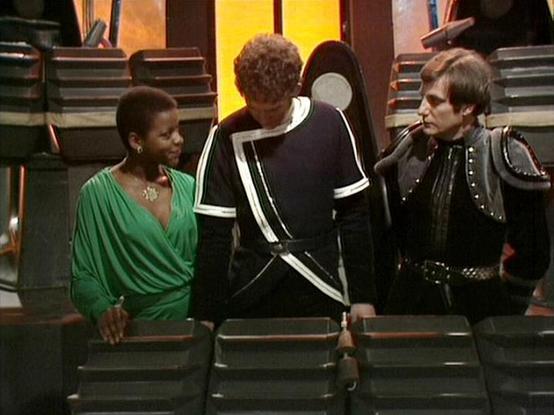 Claude Sonnet 4 describes the image as: "This image appears to be from a science fiction television production, likely from the late 1970s or 1980s based on the styling and set design. The scene takes place on what looks like a futuristic spacecraft or space station, with metallic stairs and industrial-looking architecture in the background.

Three actors are positioned on the steps in what appears to be a dramatic scene. On the left is an actress wearing an elegant emerald green dress with a d…