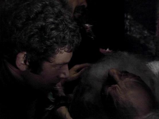 Claude Haiku 4.5 describes the image as: "# Image Description

This appears to be a scene from a science fiction television production, shot in low lighting conditions that create a dark, dramatic atmosphere. The image shows two male figures in an intimate or confrontational moment, with their faces close together in profile. The lighting is minimal, with only subtle highlights illuminating portions of their faces and upper bodies against the dark background.

The setting appears to be an inter…