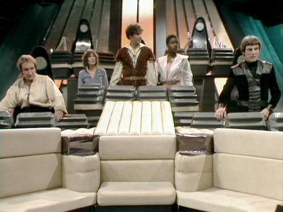 Claude Sonnet 4.5 describes the image as: "This image shows a scene from the classic British science fiction series "Blake's 7" (1978-1981). The setting is the flight deck of the Liberator, the advanced alien spacecraft that serves as the crew's base throughout much of the series.

The distinctive set features curved white seating in the foreground and an elevated platform behind with angular Art Deco-inspired panels. The crew members are positioned at their typical stations, wearing the show's…