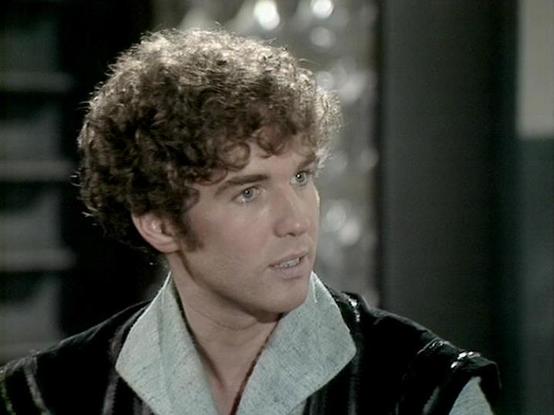 Claude Sonnet 3.7 describes the image as: "The image shows a person with curly light brown hair in what appears to be a scene from a period production. They're wearing a dark jacket with a light-colored collar or scarf visible underneath. The individual has a somewhat concerned or earnest expression and is captured in what looks like an indoor setting with a blurred background.

The scene has the visual quality of a television production from several decades ago, likely from the 1970s or 1980s …