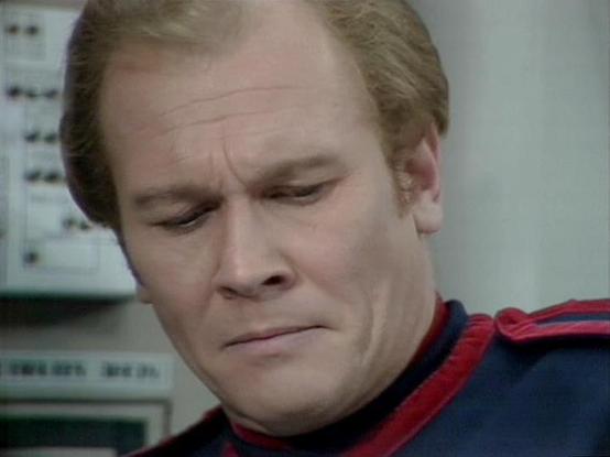 Claude Sonnet 4.5 describes the image as: "This image shows a close-up shot of a person wearing what appears to be a Starfleet uniform from Star Trek, specifically featuring the distinctive red and dark blue color scheme with shoulder piping characteristic of the franchise's costume design. The uniform style suggests this is from one of the Star Trek television series. The scene appears to be set in a technical or operations area aboard a spacecraft, with control panels and equipment visible in…