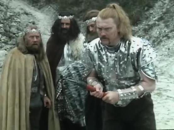 Claude Sonnet 4.5 describes the image as: "This image appears to be from a medieval or fantasy-themed film or television production, likely from the 1970s or 1980s based on the visual quality and production style. Four characters are shown standing outdoors in what appears to be a rocky, mountainous terrain with misty or foggy conditions in the background.

The figures are dressed in period costumes: one wears a tan/beige cloak or robe, another is dressed in dark clothing with fur trim, and a p…