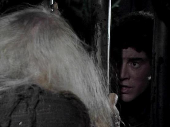 Claude Sonnet 3.7 describes the image as: "This image appears to be a still from what seems to be a film or television production, possibly from a drama or thriller. The scene is quite dark and atmospheric, creating a tense mood. On the right side of the frame, there's a person with dark hair partially visible, seeming to peer through what might be a doorway or narrow opening. On the left, there's someone with white or light-colored hair, shown from behind.

The lighting creates strong shadows …