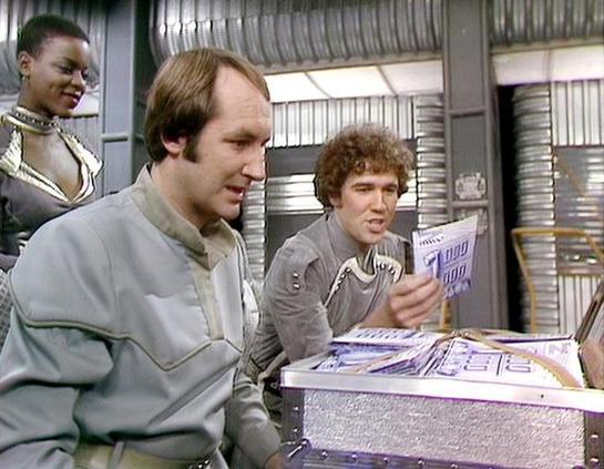 Claude Haiku 4.5 describes the image as: "# Scene from a Science Fiction Television Production

This image appears to be from a 1970s or 1980s science fiction television series, set in what looks like a spaceship's command or control center. The metallic walls, control panels with vertical striping, and technical equipment visible in the background establish a futuristic aesthetic typical of the era.

The scene shows three main figures in the foreground engaged with what appears to be technical…