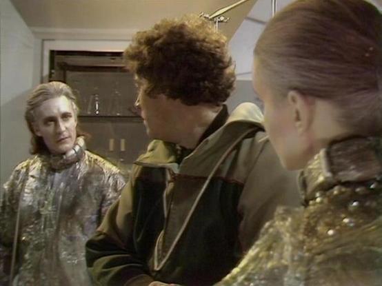 Claude Sonnet 4 describes the image as: "This image appears to be from a television production, showing three actors in what looks like a futuristic or science fiction setting. The scene takes place in what appears to be a spacecraft or advanced facility interior, with metallic walls and modern furnishings visible in the background.

The actors are wearing distinctive costumes that suggest this is from a sci-fi drama - one character wears an elaborate metallic or shimmery garment, while another…