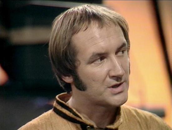 Claude Sonnet 3.7 describes the image as: "The image shows a person with short brown hair and sideburns in what appears to be a scene from a television production. They're wearing a light tan or gold-colored uniform with black striping at the collar. The background has warm tones and appears to be a set, likely from a science fiction program given the styling of the costume.

The image has a vintage quality to it, suggesting it's from a television production from the 1970s or early 1980s. The l…