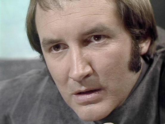 Claude Haiku 4.5 describes the image as: "I can see this is a close-up portrait of a man with distinctive features including receding hair, a beard, and intense facial expression. He appears to be in an indoor setting with a neutral background. The image quality and color grading suggest this is from a television production, likely from the 1970s or 1980s based on the visual style and cinematography. The subject is wearing what appears to be a dark-colored garment and is photographed in a serio…