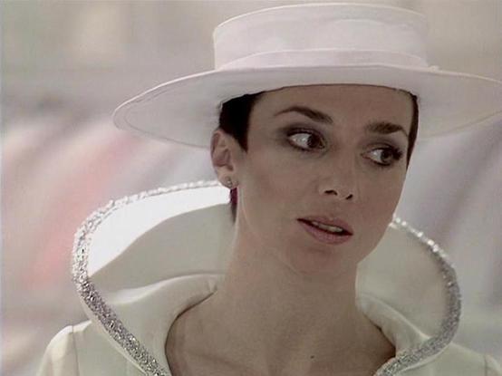 Claude Sonnet 3.7 describes the image as: "This image shows a person wearing an elegant white outfit with a distinctive high collar adorned with silver embellishment. They're also wearing a matching white wide-brimmed hat. The costume has a sophisticated, futuristic quality to it, suggesting this might be from a science fiction or fantasy production. The setting appears to be indoors with a soft, muted background.

The costume design is quite striking, with clean lines and the dramatic contrast…