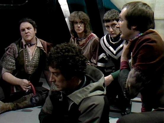 Claude Sonnet 3.7 describes the image as: "This image appears to be from the classic British science fiction television series "Blake's 7," showing a group of characters gathered in what looks like the interior of a spacecraft or control room. The scene has the distinctive visual style of late 1970s/early 1980s British television production, with somewhat muted lighting and practical set design.

The image captures what seems to be a tense moment or discussion, with several people gathered arou…