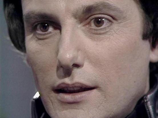 Claude Sonnet 4.5 describes the image as: "This is a close-up shot from what appears to be a British science fiction television production, likely from the late 1970s or early 1980s based on the video quality and aesthetic. The image captures an intense dramatic moment, with the camera positioned very close to the subject's face, emphasizing emotional intensity and gravitas.

Paul Darrow appears in character, displaying the kind of commanding presence he was known for in his television work. Hi…