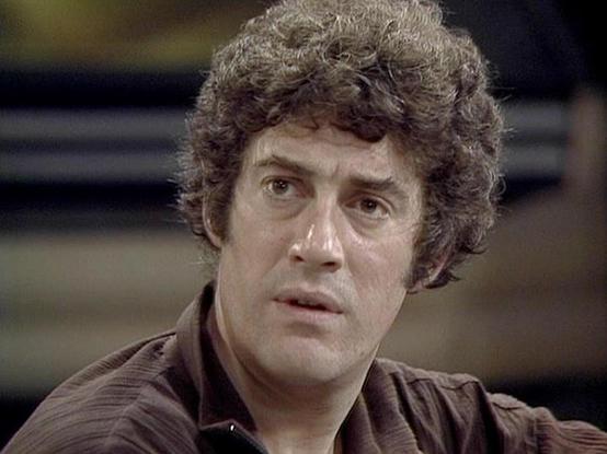 Claude Sonnet 4 describes the image as: "I can see this appears to be from a science fiction television production, likely from the late 1970s or early 1980s based on the visual quality and styling. The image shows someone with dark curly hair wearing what appears to be a brown or leather-like garment, photographed against a blurred background that suggests a spaceship or futuristic setting. The lighting and cinematography are characteristic of British science fiction television from that era. …