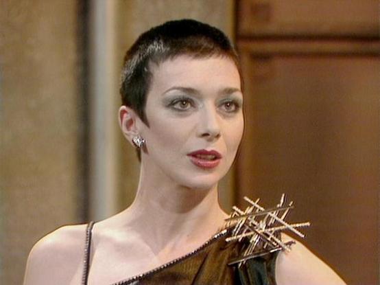 Claude Sonnet 4 describes the image as: "I can see this is an image from what appears to be a science fiction production, likely from the late 1970s or early 1980s based on the production style and costume design. The scene shows someone in an elaborate futuristic costume featuring metallic spikes or thorns on the shoulder area, creating a dramatic and intimidating appearance. The setting appears to be an interior space with warm, golden lighting and architectural elements visible in the backgr…