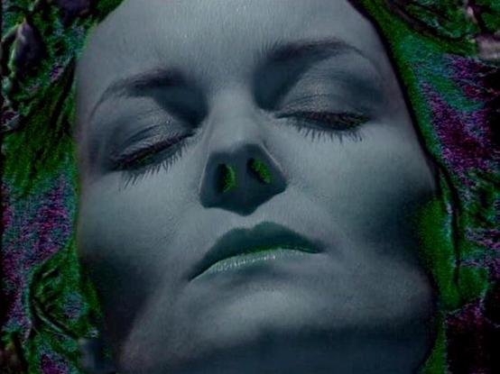 Claude Sonnet 3.7 describes the image as: "The image shows a close-up portrait with a dreamlike, ethereal quality. The subject appears to be in repose with closed eyes, giving the impression of sleep or perhaps a more symbolic state. The composition has a distinctive artistic style with a cool, blue-tinted color palette.

Surrounding the central figure are green elements that resemble foliage or natural textures, along with hints of purple, creating a surreal, almost otherworldly atmosphere. Th…