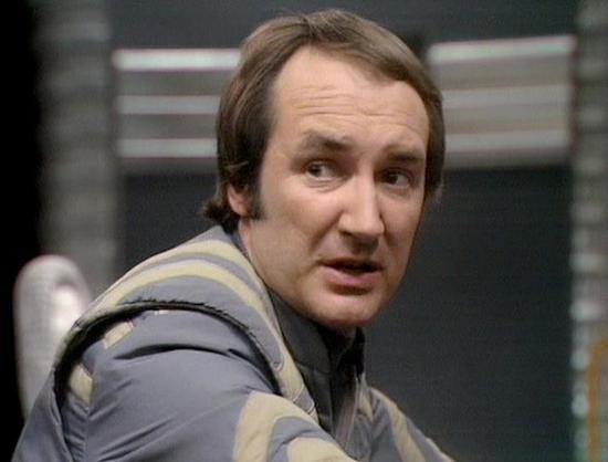 Claude Sonnet 4 describes the image as: "This image shows a scene from what appears to be a science fiction television production, likely from the late 1970s or early 1980s based on the visual style and production quality. The setting appears to be inside a futuristic spacecraft or space station, with characteristic metallic corridors and technical equipment visible in the background.

The person in the image is wearing a distinctive costume consisting of a form-fitting outfit in muted tones of…