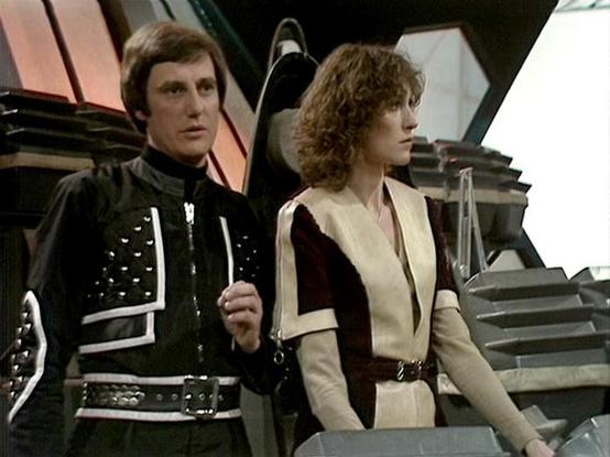 Claude Haiku 4.5 describes the image as: "# Science Fiction Scene

This image captures a scene from a classic science fiction television production, featuring two characters in elaborate futuristic costumes. The setting appears to be a spacecraft or space station interior, with geometric architectural elements visible in the background.

On the left stands a figure wearing a striking black outfit adorned with silver studs and geometric patterns, complemented by a distinctive belt. This characte…