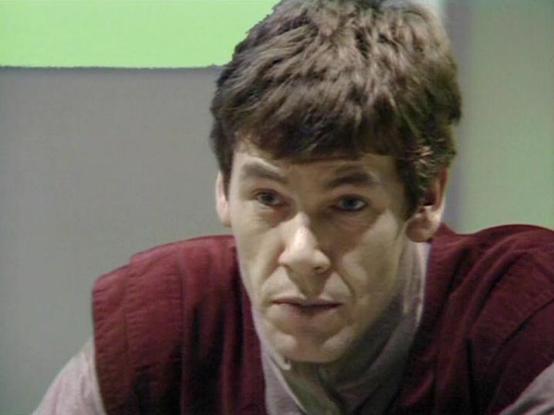 Claude Sonnet 4.5 describes the image as: "This image shows a close-up shot of actor Michael Halsey in what appears to be a scene from a television production, likely from the 1980s or early 1990s based on the video quality and aesthetic. He is wearing a burgundy or maroon colored jacket over what looks like a grey or mauve shirt. His expression is intense and somewhat confrontational, with raised eyebrows and a slight grimace, suggesting he's in the middle of a dramatic or tense scene.

The se…