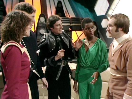 Claude Haiku 4.5 describes the image as: "This image appears to be from a science fiction television production, likely from the 1980s based on the styling and set design. The scene takes place on what looks like a spaceship bridge or command center, with distinctive futuristic set pieces visible in the background including geometric panels and atmospheric lighting in yellows and teals.
Five actors are present in the scene, engaged in what appears to be a dramatic conversation or confrontation…